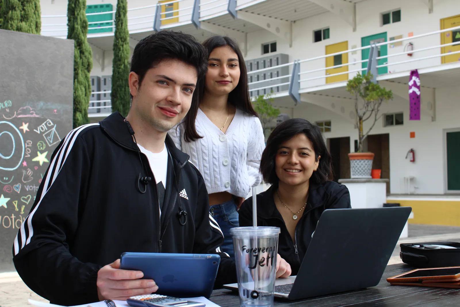 Alumnos de Bachillerato trabajando juntos con tableta y laptop en el campus
